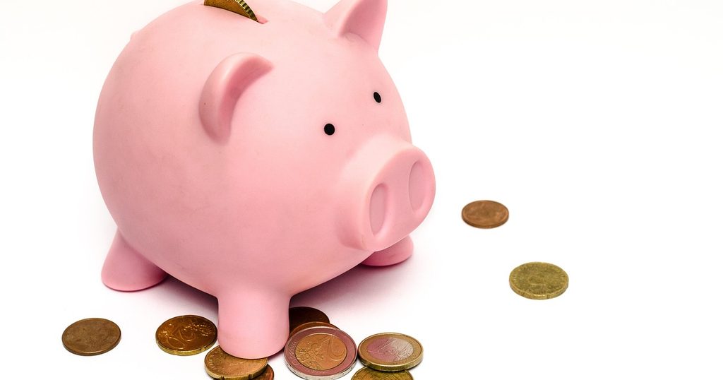 白い台の上のピンクの豚の貯金箱と散らばった硬貨