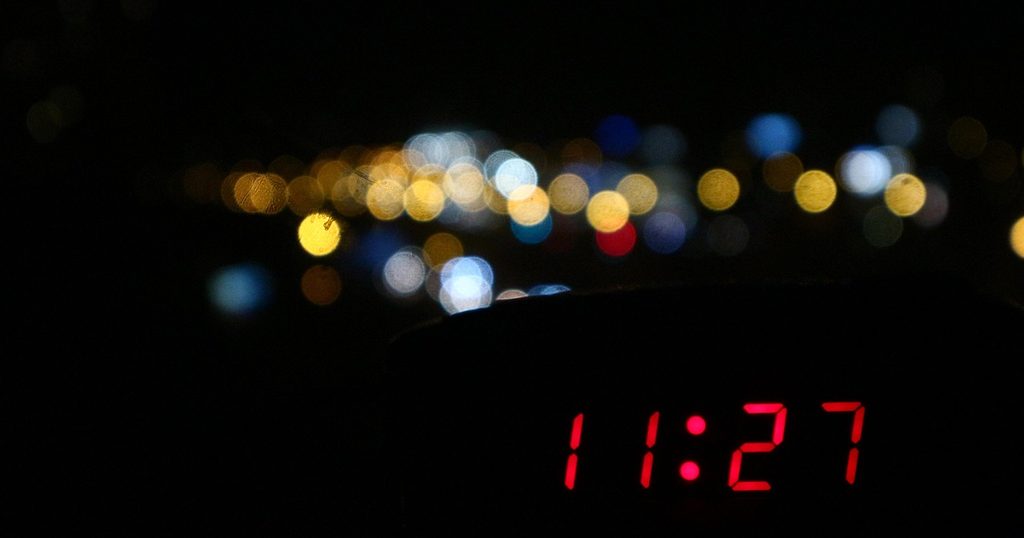 夜の街の明かりを背に、赤い数字が光るデジタル時計
